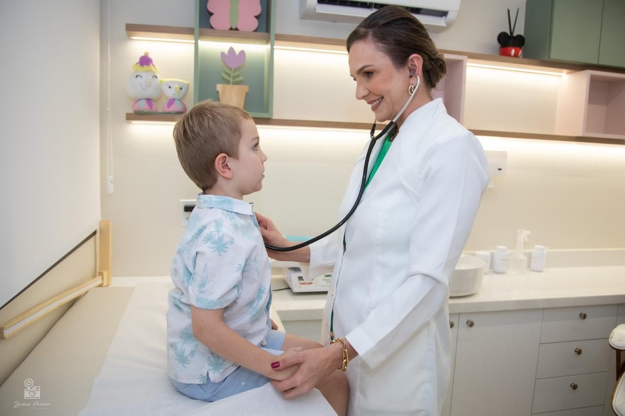 Dra. Helen Osterne auscultando um menino sentado na maca do consultório