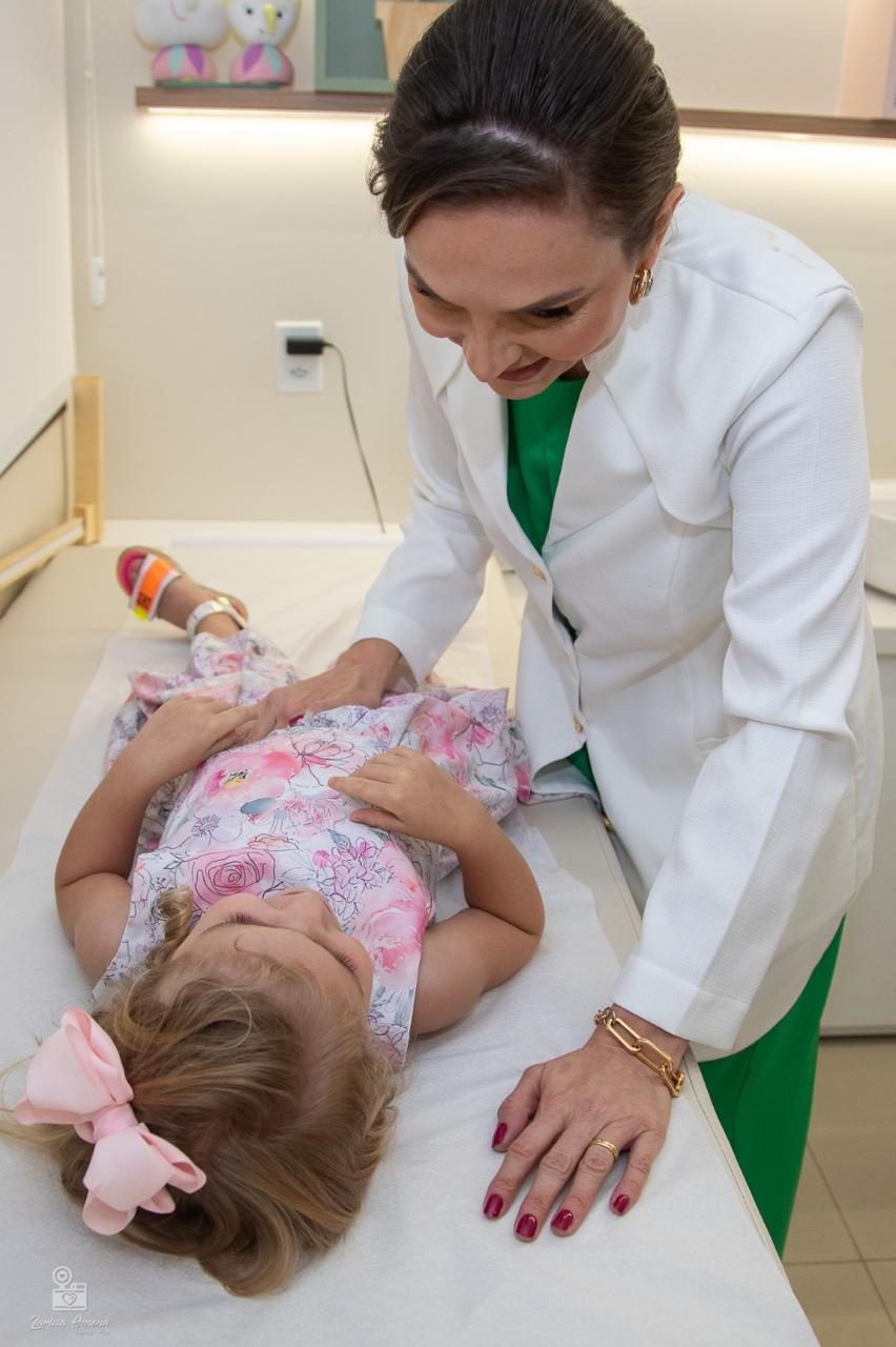 Dra. Helen Osterne examina a barriga de uma menina deitada na maca do consultório
